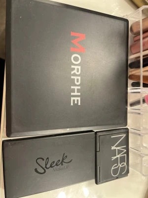 Ögonskuggspaletter Morphe, Sleek & NARS - Tre ögonskuggspaletter från Morphe, Sleek MakeUP och NARS. Morphe-paletten har nio matta och skimriga nyanser i varma bruna och beige toner. Sleek och NARS har mindre paletter med persiko- och nude-färger. Alla i smidiga svarta plastförpackningar.