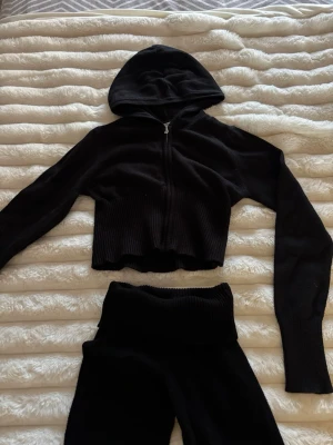 Svart tröja och byxor från Gina Tricot - Svarta mjukisbyxor/yogapants från Gina Tricot i mjukt och stretchigt tyg. Byxorna har ribbade detaljer. Perfekta för en chill och avslappnad stil. Matchande svart hoodie med dragkedja och huva.  Det är barnstorlek men passar mig som brukar ha xs. Mått: innerbenslängd 73cm, midjan på tröjan 30cm.