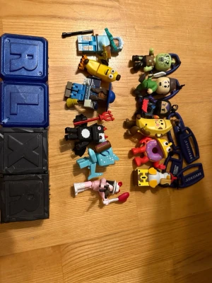 Samling Roblox-figurer och nyckelringar - Säljer en samling med färgglada Roblox-figurer och nyckelringar. Figurerna föreställer olika karaktärer som banan, zombie, pingvin och andra roliga former. Materialet är plast och flera av figurerna har tillbehör eller detaljer som vapen och hattar. Perfekt för dig som gillar Roblox eller vill ha coola samlarprylar.