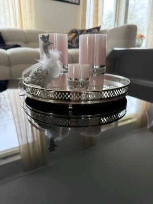 Lene Bjerre  - Säljer ett runt silverfärgat dekorationsfat med spegelbotten, tre ljusrosa blockljus med silverdekor och en glittrig påfågel med vita fjädrar. Perfekt som snygg inredningsdetalj till vardagsrummet eller som centerpiece på soffbordet.