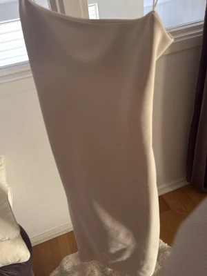 Beige långklänning med öppen rygg - Säljer en elegant beige långklänning med stilren, rak passform och öppen rygg. Klänningen har tunna axelband och är tillverkad i ett mjukt, slätt material som ger en lyxig känsla. Perfekt för dig som vill ha en minimalistisk och chic look.