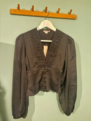 Svart blus med spetsdetaljer - Svart blus med spetsdetaljer. Helt ny och aldrig använd! Säljer pga att den är för liten 