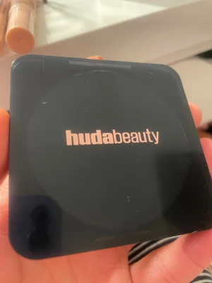Huda Beauty Easy Bake Pressed Powder - Snygg kompakt foundation från Huda Beauty i nyansen Pound Cake. Pudret är mattande och ger en airbrush-effekt. Förpackningen är svart och stilren med loggan i guld. Perfekt för att fixera sminket och få en jämn finish. !Endast provad 1-2 gånger!