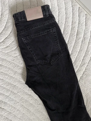 Svarta jeans  - Säljer ett par svarta  jeans från Pull&Beae. Jeansen har hög midja, raka ben och en slits längst ned. Referens: jag är 180 cm (dem är precis ovanför golvet)