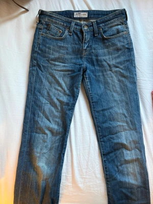Blå raka jeans från Lee - Säljer ett par klassiska blå jeans från Lee med rak passform och fem fickor. Jeansen har en snygg tvättad look och detaljer i kopparfärgad metall. Perfekta för en avslappnad stil och passar till det mesta.