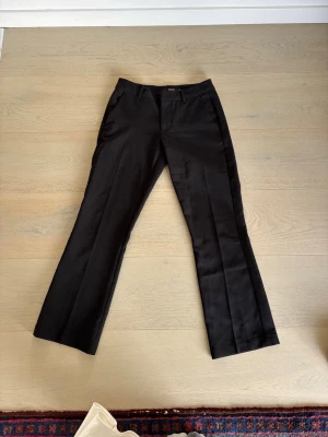 Svarta lågmidjade kostymbyxor från Bik Bok - Populära lågmidjade kostymbyxorna från bikbok! Snygga svarta kostymbyxor från Bik Bok med bootcut ben och pressveck. Byxorna har hällor för skärp, sidofickor och stängs med knapp och dragkedja. Perfekta för en clean och stilren look.