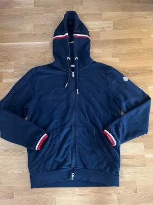 Moncler hoodie  - Snygg och fräsch Moncler hoodie! Kan inte med säkerhet garantera att den är äkta men jag tror det😁Jag tror den är i strl Large, passar iallafall mig som är 186. Den har inga defekter och inte jätteanvänd. Skriv om du vill ha fler mått eller svar på frågor☺️