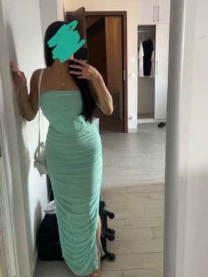 Mintgrön bandeauklänning Rare London - Mintgrön bandeauklänning från Rare London med korsettliknande överdel och smala axelband. Klänningen har en figurnära passform, slits på sidan och är tillverkad i ett lätt, stretchigt material. Perfekt för sommarens alla tillfällen.