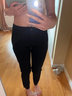 Svarta kostymbyxor Capri Collection - Snygga svarta kostymbyxor från Capri Collection med smal passform och hög midja. Byxorna har knapp och dragkedja framtill och är tillverkade i ett stretchigt material som sitter bekvämt. Perfekta för en clean och stilren look. Oanvänd.  Fint skick.  Storlek: S en liten M kan definitivt också ha de. Stretchiga.  Kant till kant: 39cm  Stussen: 50cm  Beninnerlängdsmått: 70-71cm  Material: se sista bild.  Pris kan diskuteras.  Om du vill veta om modellens längd och vikt så står det i profilen.