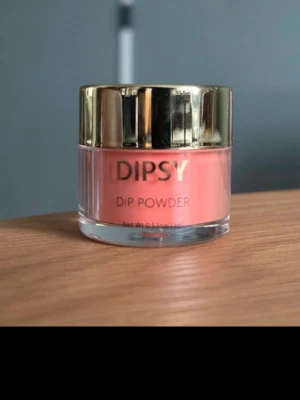 DIPSY Dip Powder Caramel Appel - DIPSY Dip Powder i färgen Caramel Appel är ett snyggt dip-pulver för naglar i en mjuk karamellrosa nyans. Kommer i en rund burk med guldfärgat lock. Perfekt för dig som vill ha en modern och fräsch look på naglarna. Pulvret ger ett jämnt och täckande resultat.