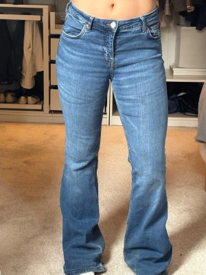 Bootcut jeans - Säljer ett par klassiska blå bootcut jeans med medelhög midja och fem fickor. Jeansen har en snygg tvätt och utsvängda ben, perfekta till sneakers eller boots. Stängs med knapp och dragkedja. Materialet är mjukt denim i bomull. Lite slitna där nere, därav priset. Annars i fint skick💙