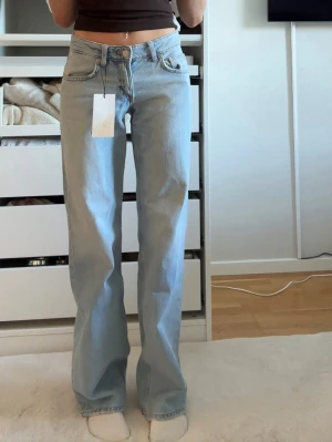 Ljusblå raka jeans  - Säljer ett par ljusblå jeans med rak passform och låg midja. Jeansen har klassiska fem fickor, bälteshällor och stängs med knapp och dragkedja. Materialet är denim i bomull och de har en avslappnad, trendig look. Från Zara, Stl 32. Helt nya med prislapp kvar! Köpta för 399
