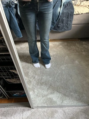 Blå bootcut jeans med låg midja - Säljer ett par blå bootcut jeans med låg midja och klassisk femficksmodell. Jeansen har snygga slitningar framtill och är tillverkade i stretchigt denimtyg för skön passform. Perfekta till sneakers eller boots. Dessa är helt oanvända så i fint skick och nypris är 699kr🩷