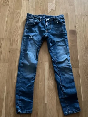 Blå skinny jeans från Dsquared2 - Säljer ett par blå skinny jeans från Dsquared2 med slitningar och snygga detaljer. Jeansen har klassisk femficksmodell, knappgylf och kontrastsömmar. Tillverkade i denim med en cool tvätt och Dsquared2-logga på den röda etiketten vid gylfen.