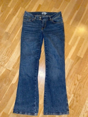 Blå bootcut jeans från 157 - Ett par klassiska blå bootcut jeans från 157 med fem fickor och snygga kontrastsömmar. Jeansen har normalhög midja och lätt utsvängda ben. Perfekta för en avslappnad och trendig look. Tillverkade i denim med en autentisk tvätt. Använda vid ett tillfälle, så gott som nya! 