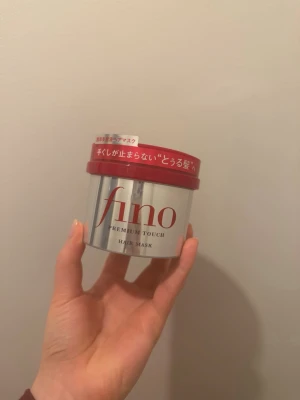 Fino Premium Touch hårinpackning - Fino Premium Touch hårinpackning i en silvrig burk med rött lock. Produkten är en hårmask som ger intensiv vård och glans till håret. Förpackningen har japansk text och är tillverkad i plast. Perfekt för dig som vill boosta håret med extra fukt och näring.