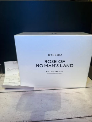 Byredo Rose of No Man's Land parfym - Byredo Rose of No Man's Land Eau de Parfum i elegant vit kartong med svart text. Parfymen har en modern och stilren design, perfekt för dig som gillar exklusiva dofter och minimalistisk estetik. Förpackningen är rektangulär och känns lyxig.