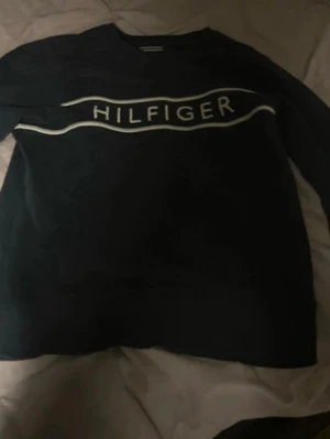 Mörkblå sweatshirt från Tommy Hilfiger - Snygg svart sweatshirt från Tommy Hilfiger med vit logga. Klassisk rund halsringning och långa ärmar. Perfekt för en avslappnad och trendig look. Den e i storlek 152.