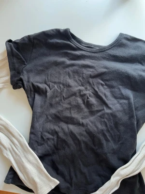 Svart layering-topp Brandy Melville - Säljer en svart layering-topp från Brandy Melville med rund halsringning och långa, ribbade vita ärmar i kontrastmaterial. Toppen är i mjuk bomull och har en avslappnad passform, perfekt för att skapa en cool lager-på-lager-look.