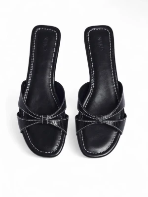 Svarta slip-in sandaler från NA-KD - Säljer ett par svarta slip-in sandaler från NA-KD med fyrkantig tå och låg klack. Sandalerna har korsade remmar i glansigt material och vita kontrastsömmar runt sulan. Perfekta för en trendig och stilren look.