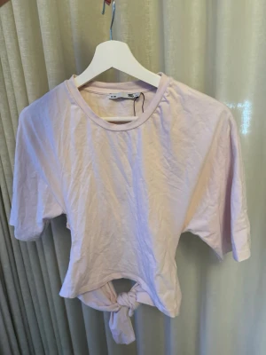 Ljusrosa croppad topp med knyt - Säljer en ljusrosa knyt tröja från lager som andvänt en gång och legat i garderob! Den är liten i storlek och skysterbar! Säljer pga ingen andvändning! Kan stryka innan jag skickar om köparen vill!🩷