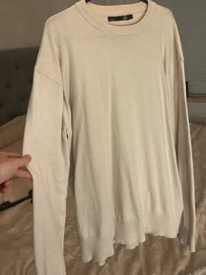 Beige stickad tröja från lager 157 - En stilren beige stickad tröja från H&M med rund halsringning och långa ärmar. Tröjan har en enkel och avslappnad passform med ribbade muddar vid ärmslut och nederkant. Perfekt att matcha med jeans e för en clean look.