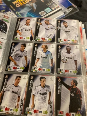 Samling Real Madrid fotbollskort från 2012/2013  - Säljer en samling fotbollskort med spelare från Real Madrid, UEFA Champions League. Korten har svart och vit design med spelare i vita matchtröjor och klubbens logga. Perfekt för dig som gillar att samla på fotbollskort och är fan av Real Madrid.
