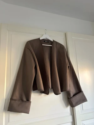 Brun cardiganjacka - Säljer en brun oversized tunn cardiganjacka med vida ärmar. Jackan har öppen front med knappar och dekorativa sömmar längs kanterna🤎Aldrig använd men ej prislapp kvar. 