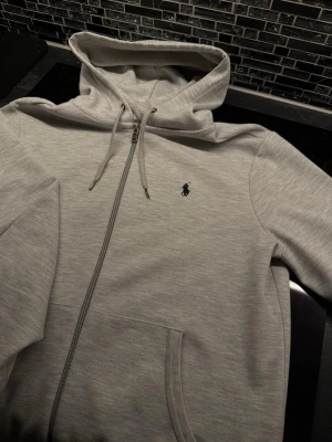 Polo Ralph Lauren zip-hoodie  - Klassisk ljusgrå hoodie med dragkedja från Polo Ralph Lauren. Klassisk och fräsch design som passar allt, två fickor framtill och den ikoniska broderade loggan på bröstet. Perfekt för en chill och stilren look.