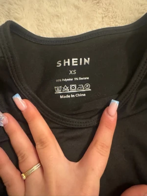 Svart croppad långärmad topp SHEIN - Snygg svart croppad långärmad topp från SHEIN i stretchigt material. Tillverkad av 95% polyester och 5% elastan, perfekt för att matcha med höga jeans eller kjol. Enkel och stilren design med rund halsringning.