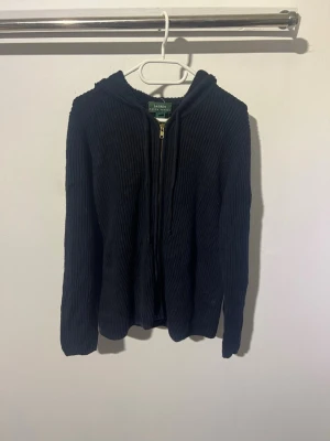 Svart ribbad hoodie från Lauren Ralph Lauren - Säljer en svart ribbad hoodie från Lauren Ralph Lauren med dragkedja framtill och huva. Hoodien har långa ärmar och är tillverkad i ett mjukt, stretchigt material som ger en skön passform. Perfekt för en avslappnad och stilren look.