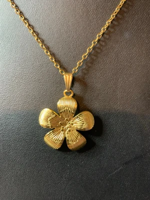 Guldigt halsband med blomma - Snyggt halsband i guldfärg med ett stort blomformat hänge. Hänget har fem kronblad med räfflad yta som ger en cool struktur. Kedjan är tunn och matchar hängets färg perfekt. Perfekt accessoar för dig som vill sticka ut med en unik detalj.