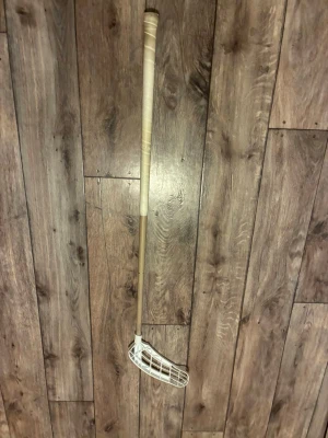 Salming klubba med ett beiget skaft och ett vitt blad - Innebandyklubba med beige skaft och vitt plastblad. Skaftet är rakt och har ett greppvänligt handtag. Bladet är gallerformat och tillverkat i tålig plast, perfekt för snabba passningar och skott.