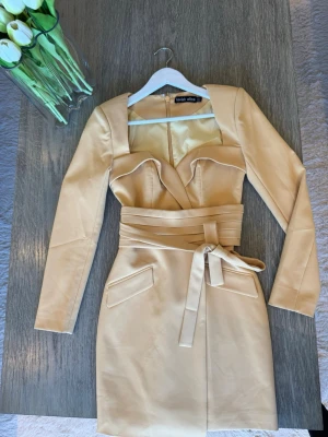 Gul klänning perfekt till påsken  - Snygg gul kort klänning från Lavish Alice med långärmad design och markerad midja med bred knytbälte. Klänningen har unika detaljer vid bysten och två fickor framtill. Perfekt för dig som vill sticka ut med en elegant och modern look. Använd en gång. Köpt för 1200kr 