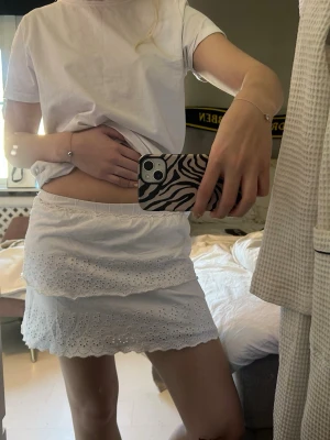 Vit kort kjol med broderade volanger från zara - Supersöt vit kort kjol med två lager volanger och broderade spetsdetaljer. Kjolen har resår i midjan för skön passform och är perfekt för varma dagar. Materialet känns lätt och luftigt, vilket gör den idealisk till sommaren.