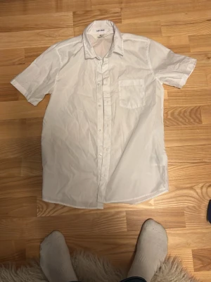 Vit kortärmad skjorta från H&M -  vit skjorta från H&M med korta ärmar och bröstficka. Skjortan har knappar framtill och är tillverkad i ett lätt och bekvämt material.