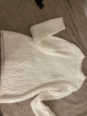 Vit fluffig stickad tröja - Mysig vit stickad tröja med fluffig och texturerad yta. Tröjan har rund halsringning och långa ärmar, perfekt för kyliga dagar. Materialet känns mjukt och ger en avslappnad look.