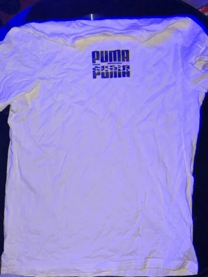 Vit Puma t-shirt med tryck - Vit t-shirt från Puma med svart tryck på ryggen där det står 'PUMA FUNK' i grafisk stil. Klassisk passform och rund halsringning. Perfekt för dig som gillar sportiga och stilrena plagg.