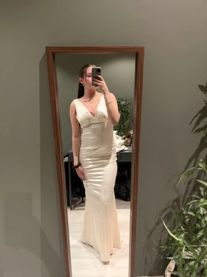 Lång champagnefärgad klänning - Elegant långklänning i champagnefärgat tyg med v-ringning och breda axelband. Klänningen har en smickrande figurnära passform och öppen rygg. Perfekt för speciella tillfällen där du vill sticka ut. Klänning är enbart testad med lappen kvar. På mig som är 171 cm lång går den enda ner till golvet💞