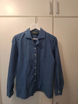 Blårutig Peak Performance skjorta - Snygg blårutig skjorta från Peak Performance med klassisk krage och vita knappar. Skjortan har lång ärm och är tillverkad i ett mjukt bomullstyg..