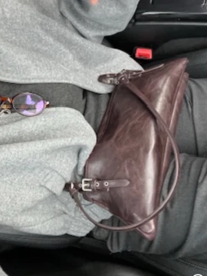 Mörkbrun/ vin röd  kuvertväska i läder - Snygg mörkbrun kuvertväska i äkta läder med avtagbar axelrem och spänndetaljer. Väskan har en stilren, avlång form och passar perfekt till dig som gillar minimalistisk design. Perfekt accessoar för att lyfta din outfit.