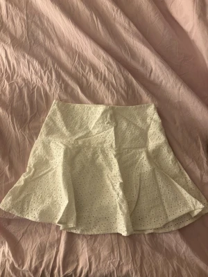 Vit kortkjol med broderade detaljer - Söt vit kortkjol med broderade blommor och volangkant. Kjolen har en lätt utsvängd form och är fodrad för extra komfort