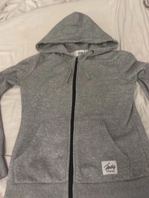 Grå zip hoodie från Andy The Road - Snygg gråmelerad hoodie med dragkedja från Andy The Road. Tröjan har huva med dragsko, två stora fickor framtill och ribbade muddar vid ärmslut och nederkant. Perfekt för en avslappnad och cool stil.