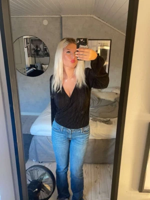 Svart ribbad topp med v ringning  - Säljer en svart ribbad topp med v-ringning och lång ärm. Toppen har en plisserad struktur som ger en snygg effekt och är tillverkad i ett mjukt, stretchigt material. Perfekt att styla med jeans eller kjol för en trendig look.