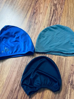Tre badmössan  - Säljer tre enkla badmössor i olika färger: en blå från Biko i glansig satin, en grå i mjuk och en svart i satinliknande material. 