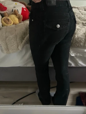 Svarta utsvängda jeans från Gina Tricot - Säljer dessa bootcut jeans med detaljer på fickorna. Köpa på Gina och är i storlek 38. Jeansen är utsvängda och går ner till hälen på mig som är 162. Jättebra skick🧸