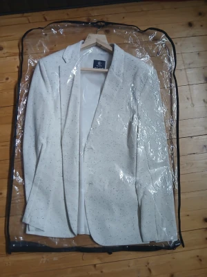 Vit kavaj (cream färg) - Stilren vit kavaj med diskreta svarta prickar. Klassisk passform med smala slag och två fickor framtill. Perfekt för en dressad look. Materialet känns lätt och andas, vilket gör den bekväm att bära. Använd 1 gång. Perfekt skick. 