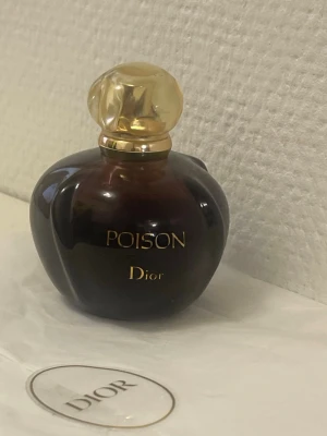 Dior Poison parfym mörklila/guld - Dior Poison parfym i en elegant, mörklila glasflaska med rundad form och guldfärgat lock. Flaskan har en lyxig känsla med guldfärgad text och klassisk design som gör den till en ikonisk doft i parfymvärlden.