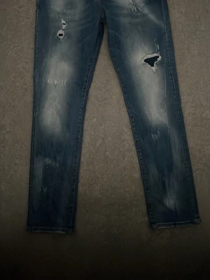 Blå slitna jeans från Dsquared2. PRIS KAN DISKUTERAS! - Säljer ett par blå jeans från Dsquared2 med slitningar och hål på benen. Jeansen har en tvättad look, raka ben och klassiska bakfickor med Dsquared2-märke. Perfekta för en cool och avslappnad stil.