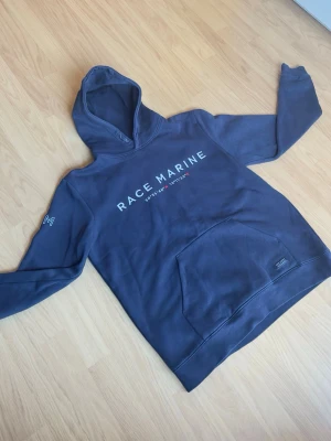 Race Marine hoodie mörkblå – storlek M - Snygg och bekväm hoodie från Race Marine i mörkblå färg. Tryck framtill samt stor framficka och mjuk insida som gör den skön att använda till vardags.  Storlek: M Färg: mörkblå Skick: bra begagnat skick  Passar perfekt till både vardag och avslappnad stil. Hör av dig vid intresse eller frågor!